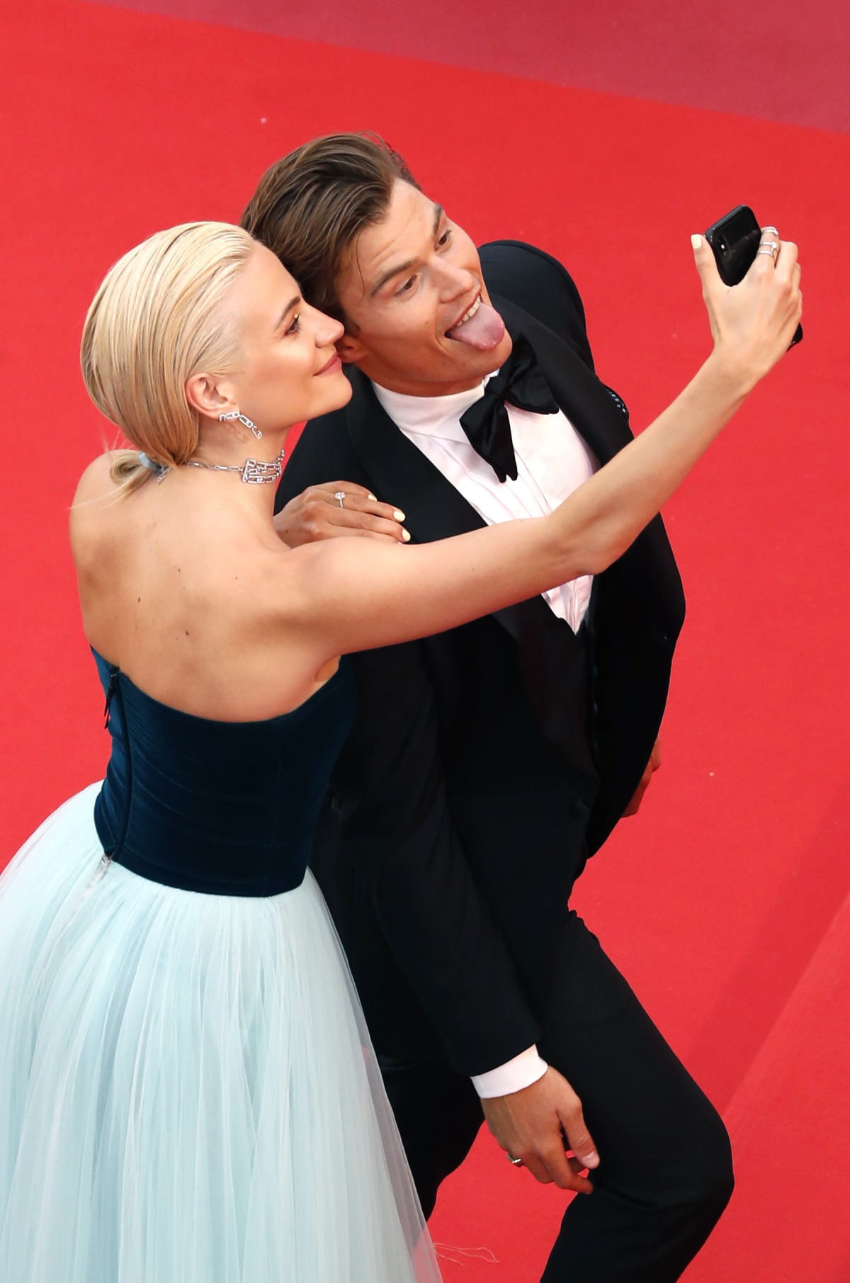 Snúbenci Pixie Lott a Oliver Chesire si robia selfie na červenom koberci. 
