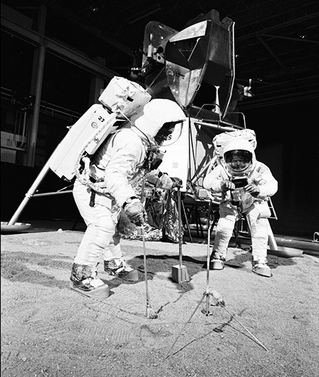Astronaut Edwin E. Aldrin Jr. (vľavo), pilot lunárneho modulu, používa na zber vzoriek odmerku a kliešte. Astronaut Neil A. Armstrong, veliteľ Apollo 11, drží tašku na prijatie vzorky - simulácia používania mesačných nástrojov na povrchu Mesiaca. Skúška sa uskutočnila počas cvičenia v budove 9 22. apríla 1969.