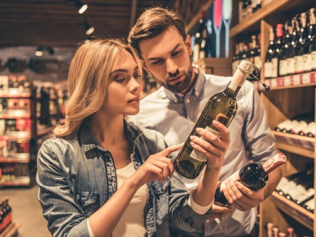 Beautiful young couple is talking and smiling while choosing wine at the supermarket